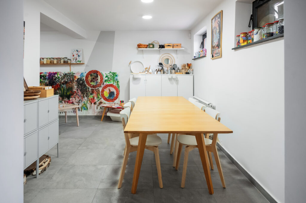 Estetycznie zorganizowana przestrzeń atelier z dużym stołem i materiałami artystycznymi – idealne miejsce do wspólnego tworzenia i rozwijania wyobraźni.